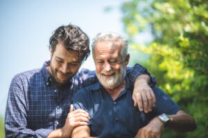 Man with his arm around smiling older father.